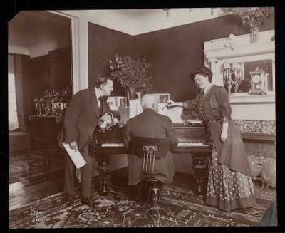Clara De Regand pointing to a score while a man plays the piano by Byron Company